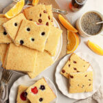 Plates of oven baked pancakes with pancake mix, topped with fruit, orange slices, coffee, and syrup on a table with flowers.