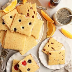 Plates of oven baked pancakes with pancake mix, topped with fruit, orange slices, coffee, and syrup on a table with flowers.