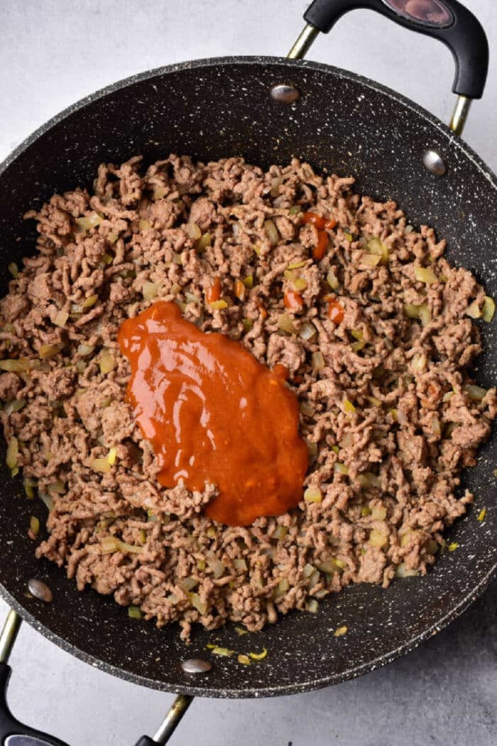 Ground beef and chopped onions sizzle in a skillet with rich red sauce on top—perfect for piling onto Texas toast sloppy joes.