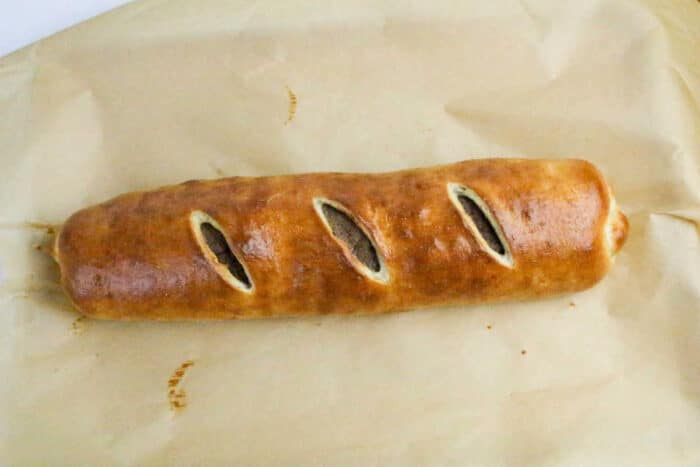 A golden-brown Philly Cheesesteak Stromboli baked pastry roll with three diagonal slits on top, resting on parchment paper.