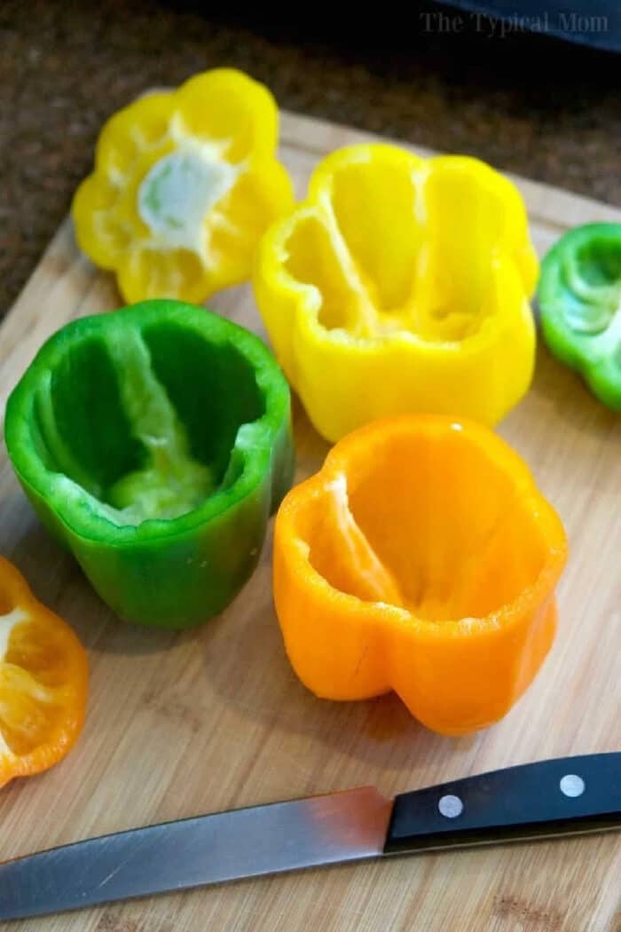 Instant Pot stuffed peppers will be your favorite pressure cooker meal! Green peppers stuffed with cheesy ground beef and rice they're packed with flavor and will bring you back to your childhood! #instantpot #pressurecooker #stuffedpeppers #crockpotexpress #instantpotrecipes #thetypicalmom Hollowed green, yellow, and orange bell peppers on a cutting board with a knife, ready for easy Instant Pot stuffed peppers.