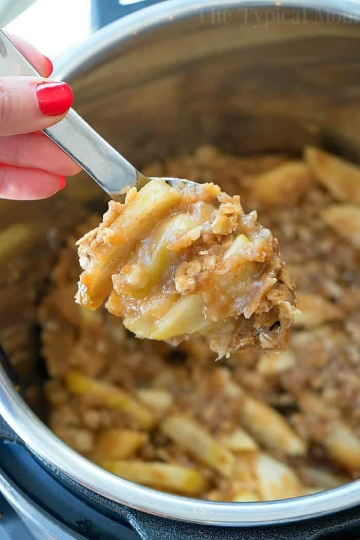 Instant Pot apple crisp recipe is amazing! Tastes like copycat Cracker Barrel baked apples we love but made in less than 20 minutes total. Warm cinnamon apples coated with a ooey gooey brown sugar glaze your family will go crazy over for sure. Try this homemade pressure cooker fruit dessert this week! #instantpot #pressurecooker #apples #applecrisp #dessert #bakedapples #instantpotrecipes #thetypicalmom #easy A spoon scoops out warm instant pot apple crisp, revealing tender apples and a golden oat topping.