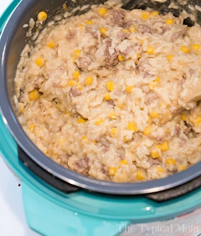 Creamy rice, ground beef, and corn mixture being stirred in a blue rice cooker—a delicious take on instant pot hamburger casserole.