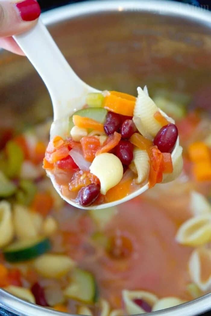 BEST Instant Pot minestrone soup recipe is full of flavor! Healthy and vegetarian too, my kids raved that this was their favorite pressure cooker soup. #instantpotrecipes #instantpot #pressurecooker #minestronesoup #vegetablesoup #soup #vegetarain #healthy #ninjafoodi #thetypicalmom A spoonful of easy Instant Pot minestrone soup with pasta shells, beans, carrots, celery, and tomatoes hovers over a steaming pot.