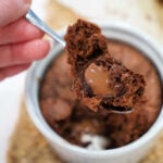 A spoon holding gooey chocolate banana bread above a ramekin filled with the same decadent dessert.