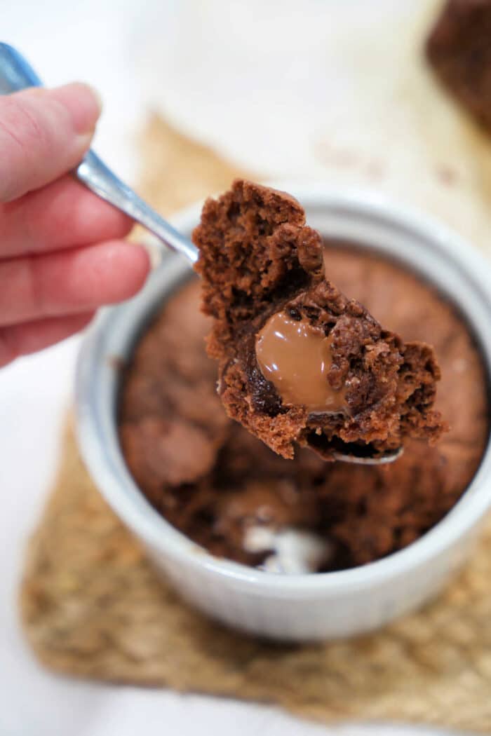 A spoon holding gooey chocolate banana bread above a ramekin filled with the same decadent dessert.