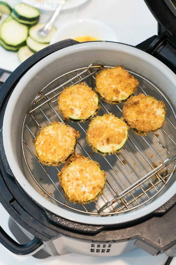 Air fried zucchini recipe! #zucchini #airfryer Six breaded air fryer zucchini chips are arranged on a rack inside an air fryer, ready to be cooked.