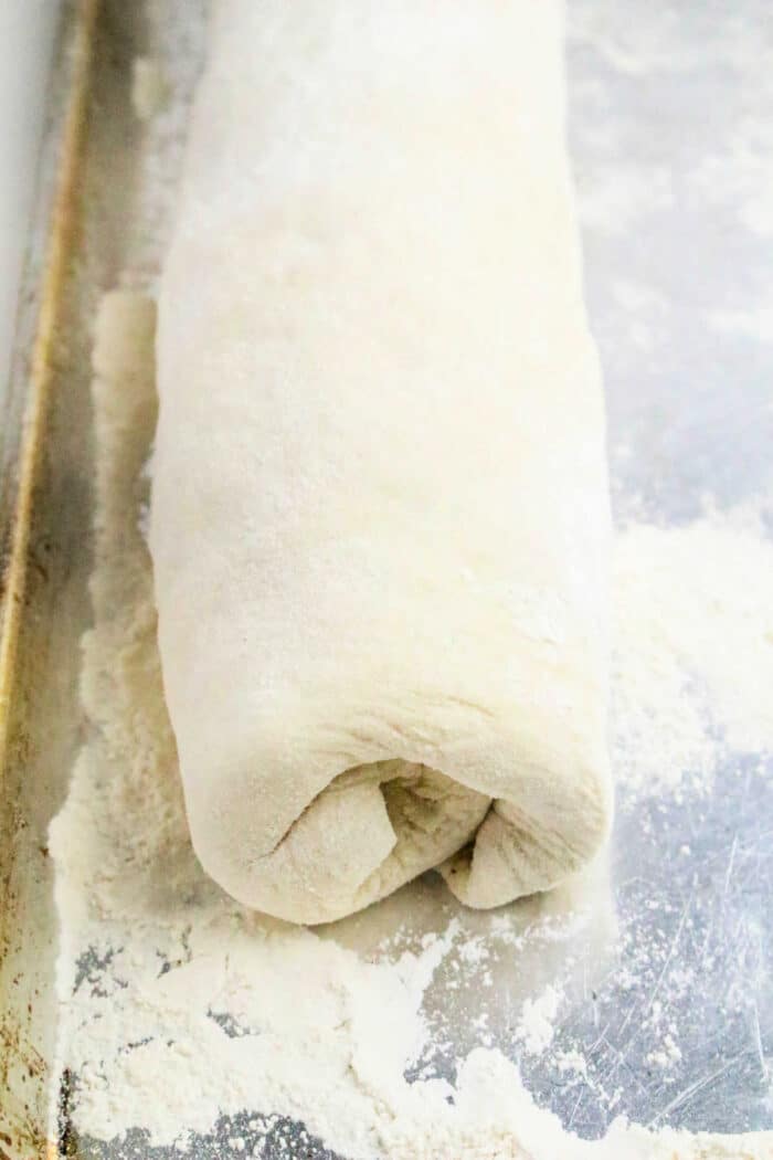 Rolled Philly Cheesesteak Stromboli dough log on a floured metal baking sheet, ready for baking.