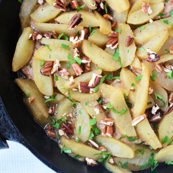 Sautéed apple slices with chopped pecans and fresh herbs in a black skillet—perfect as a topping for your favorite baked pork chops recipe or to serve alongside pork chops with apples.