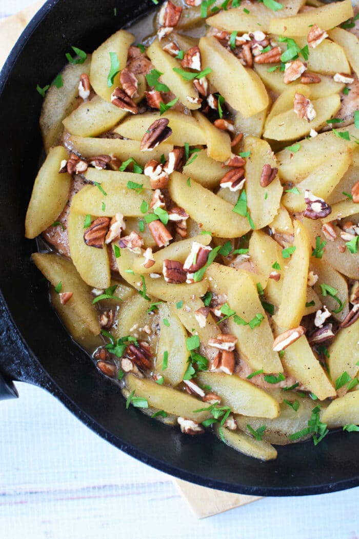 Sautéed apple slices with chopped pecans and fresh herbs in a black skillet—perfect as a topping for your favorite baked pork chops recipe or to serve alongside pork chops with apples.