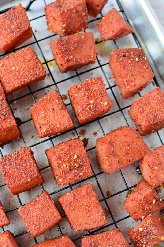 Seasoned, baked tofu cubes on a wire rack over parchment paper, inspired by BBQ burnt ends, ready to be served.