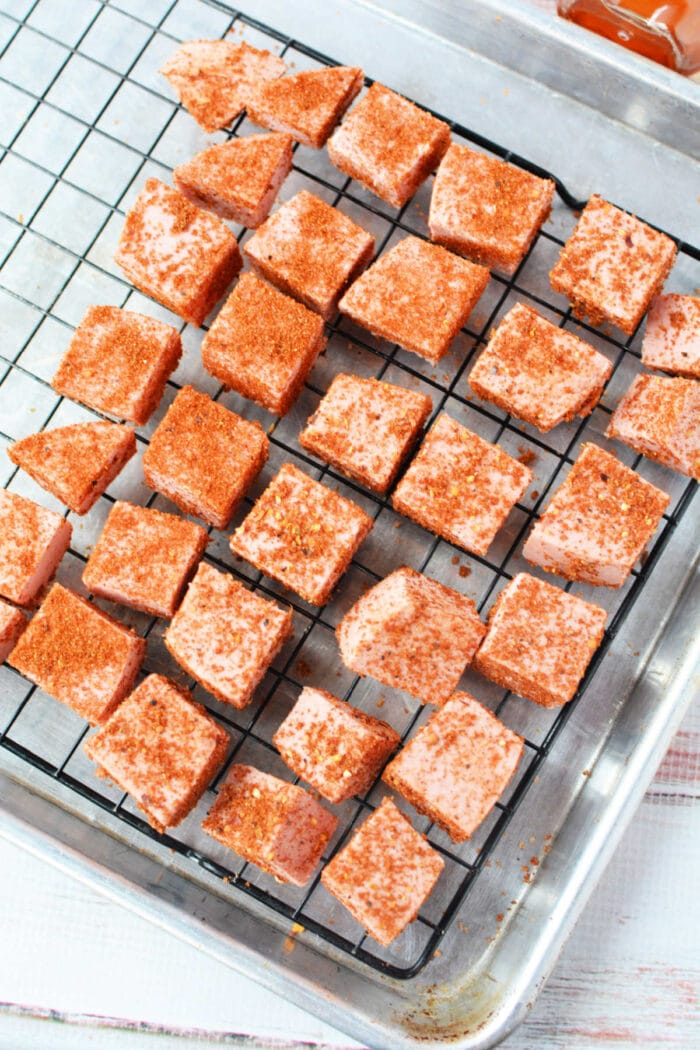 Cubes of pink candy coated with chili powder on a cooling rack over a metal baking sheet, reminiscent of Bologna Burnt Ends in their bold flavor and unique presentation.