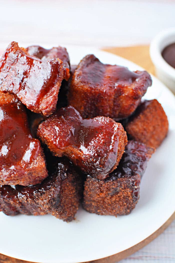 Plate of glazed, saucy pork belly burnt ends arranged in a pile on a white plate&mdash;an irresistible recipe for smoked perfection.