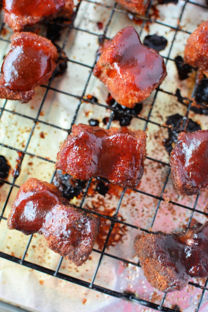 Crispy glazed pork belly burnt ends cooling on a wire rack over a foil-lined baking sheet&mdash;a mouthwatering recipe in the making.