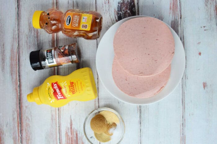 Bologna Burnt Ends on a plate, served with honey, mustard, BBQ rub, and brown sugar atop a rustic wooden surface.