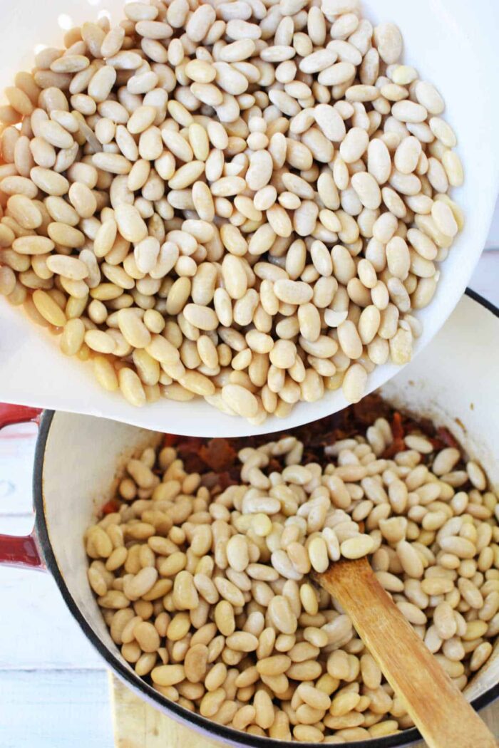 A bowl of Peruvian beans is being poured into a pot with a wooden spoon inside.
