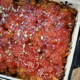A baked BBQ meatloaf topped with tomato sauce and chopped herbs in a rectangular dish.