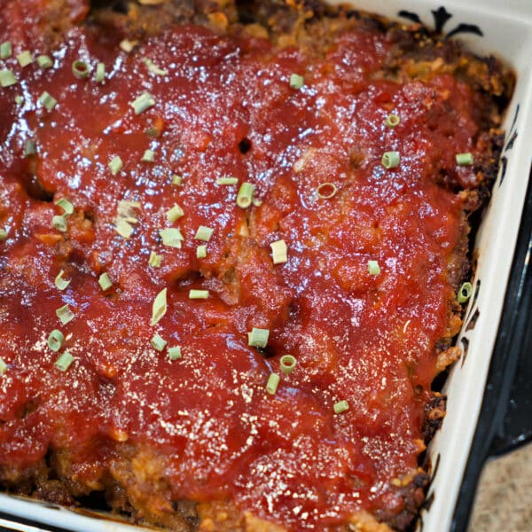 A baked BBQ meatloaf topped with tomato sauce and chopped herbs in a rectangular dish.