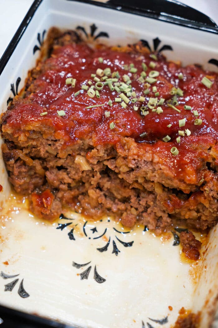 A sliced meatloaf topped with tomato sauce and herbs in a white baking dish with a black pattern, perfect for trying a classic Meatloaf Recipe or transforming into a savory BBQ Meatloaf.