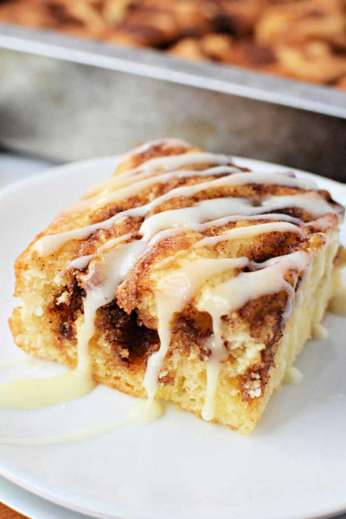 A slice of Cinnamon Roll Cake with icing drizzled on top, served on a white plate.