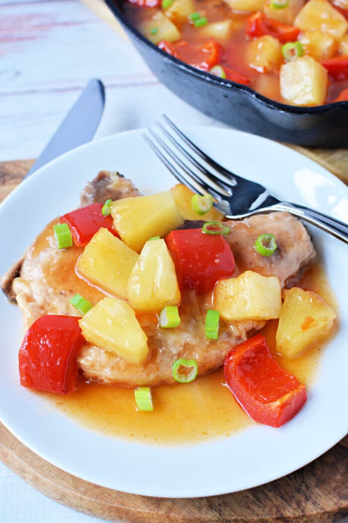 This dish features succulent pork chops topped with pineapple, red bell peppers, and sauce, then garnished with green onions on a white plate. A vibrant addition to your collection of pork chop recipes.