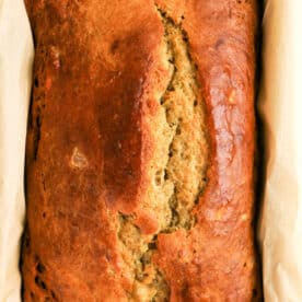 Golden brown loaf of Protein Banana Bread in a parchment-lined baking pan, viewed from above.