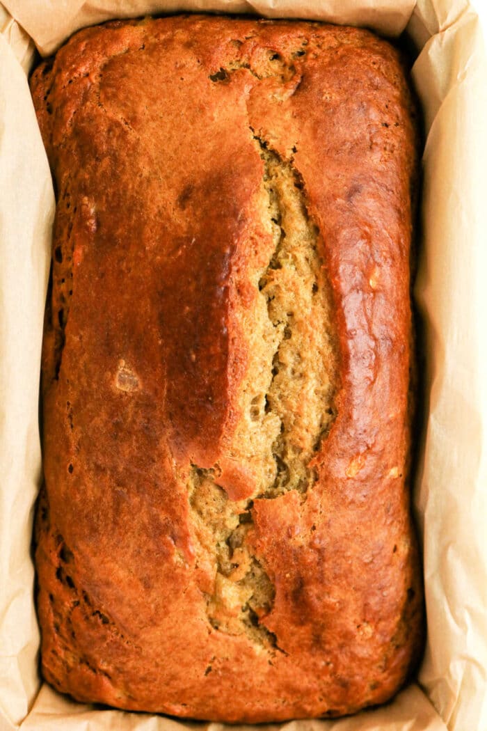 Golden brown loaf of Protein Banana Bread in a parchment-lined baking pan, viewed from above.