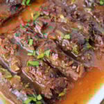 Sliced Slow Cooker Skirt Steak in rich brown gravy, garnished with chopped fresh parsley on a white serving platter.