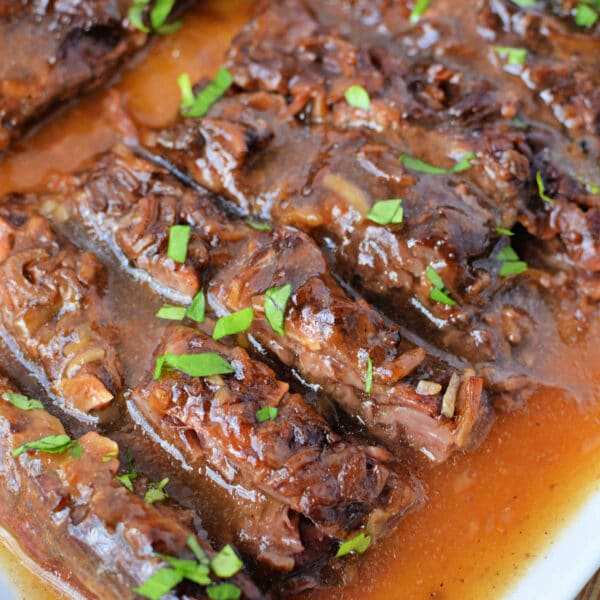 Sliced Slow Cooker Skirt Steak in rich brown gravy, garnished with chopped fresh parsley on a white serving platter.