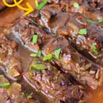 Close-up of Slow Cooker Skirt Steak in a rich sauce, garnished with chopped herbs, served on a white plate.