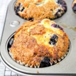 A golden-brown blueberry muffin made with blueberry muffin mix rests in a muffin tin on a cooling rack.