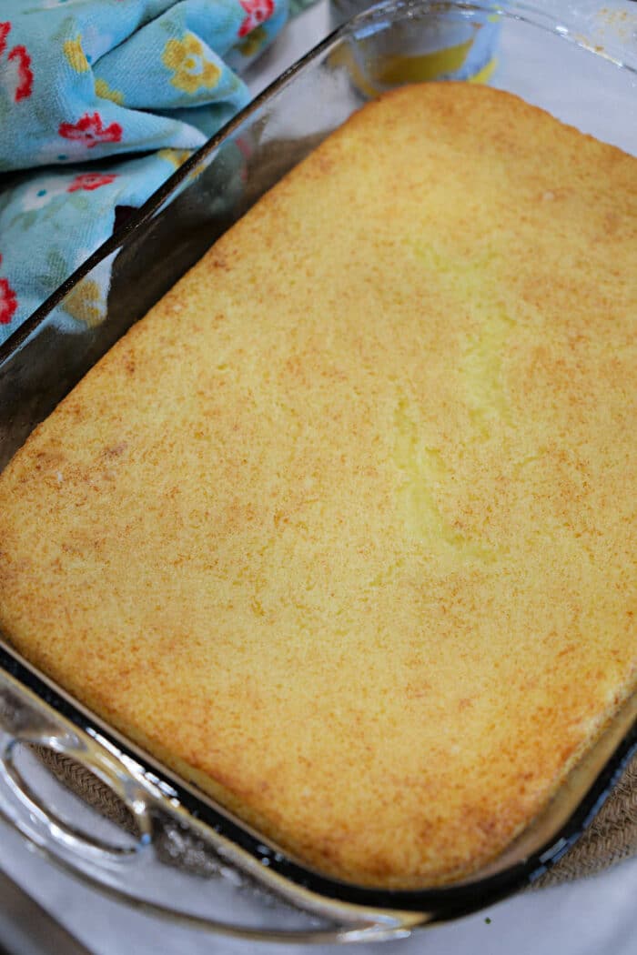 A golden-brown baked cornbread in a glass dish next to a colorful towel, perfect for pairing with your favorite carnivore meatloaf.