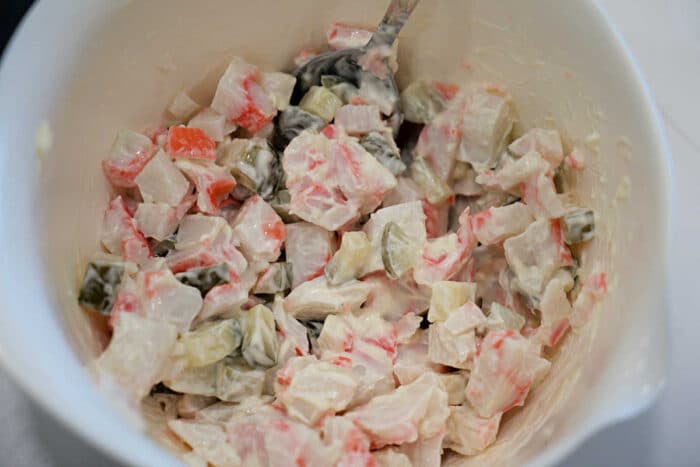 A bowl of creamy salad with diced vegetables and imitation crab, mixed with a spoon.