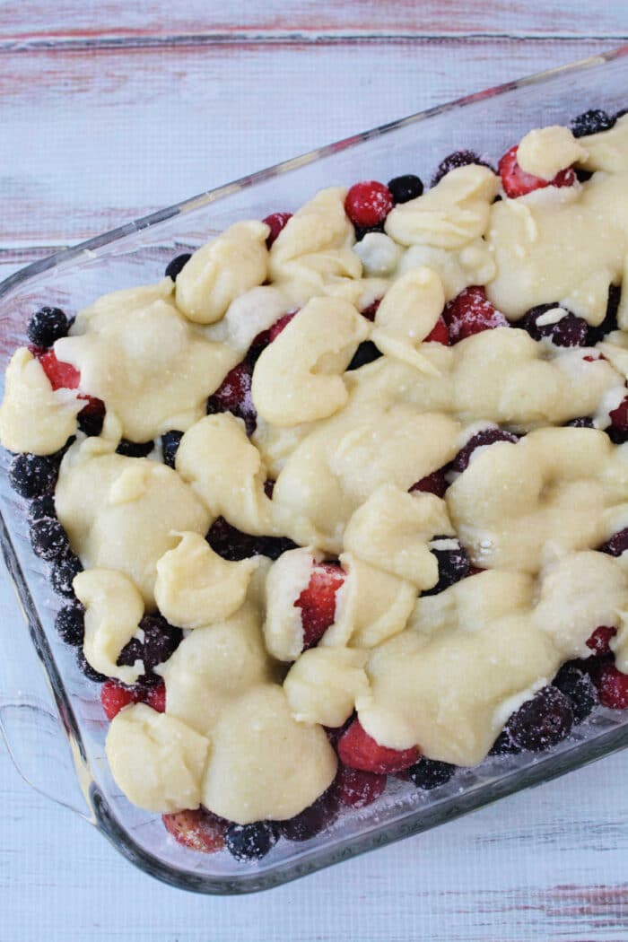A glass baking dish filled with mixed berries and blobs of unbaked dough on top, this Berry Cobbler with Cake Mix is ready to be baked for a simple, delicious dessert.