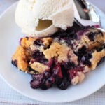 A plate with Berry Cobbler with Cake Mix and a scoop of vanilla ice cream, with a spoon beside them.