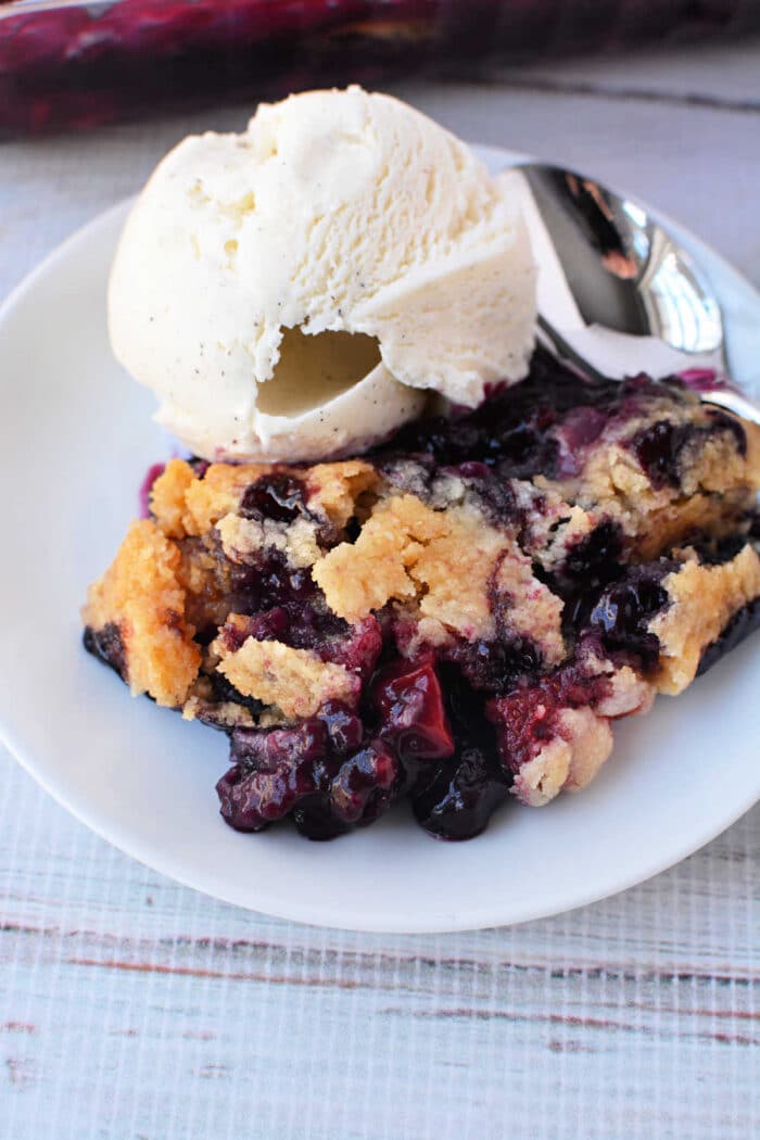 A plate with Berry Cobbler with Cake Mix and a scoop of vanilla ice cream, with a spoon beside them.