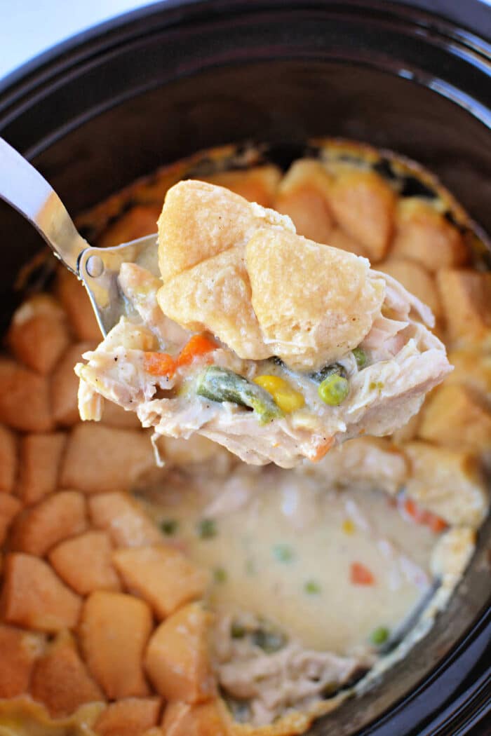 A spoon lifts creamy chicken and vegetables with biscuit topping from a slow cooker, capturing all the comforting flavors of Chicken Pot Pie in one delicious scoop.