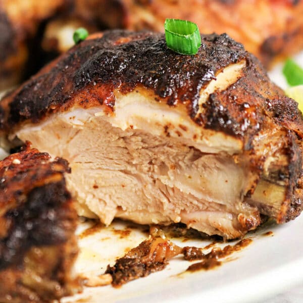 A close-up of juicy, oven jerk chicken with crispy, seasoned skin, garnished with chopped green onions.