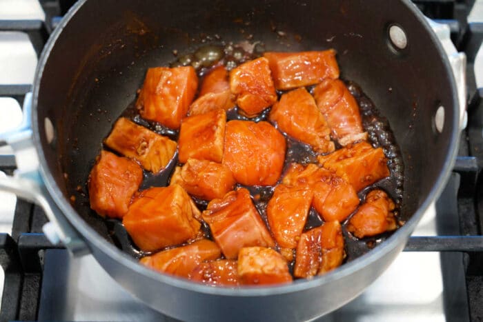 Chunks of salmon cooking in a dark teriyaki sauce in a saucepan on a stovetop—perfect for a quick Teriyaki Salmon recipe or flavorful Salmon Bites.