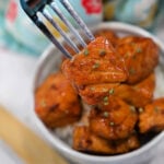 A fork holds a piece of glazed tofu above a bowl filled with more tofu pieces and rice, offering a plant-based twist on classic Teriyaki Salmon Bites.