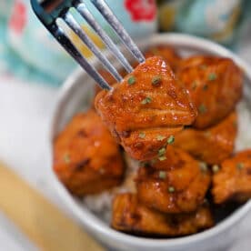 A fork holds a piece of glazed tofu above a bowl filled with more tofu pieces and rice, offering a plant-based twist on classic Teriyaki Salmon Bites.
