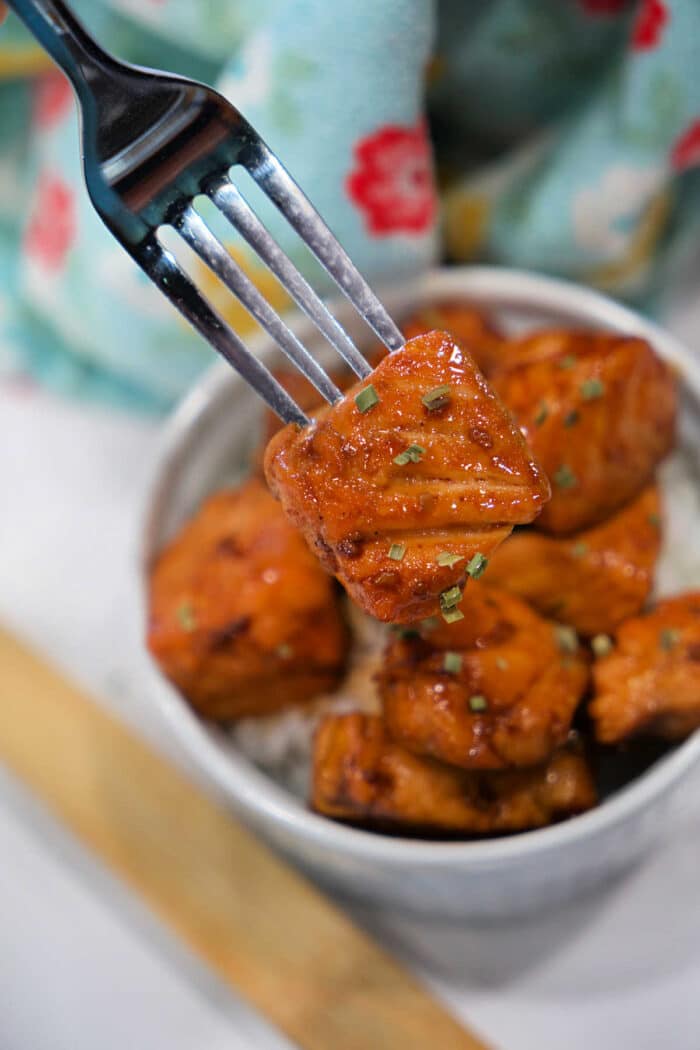 A fork holds a piece of glazed tofu above a bowl filled with more tofu pieces and rice, offering a plant-based twist on classic Teriyaki Salmon Bites.