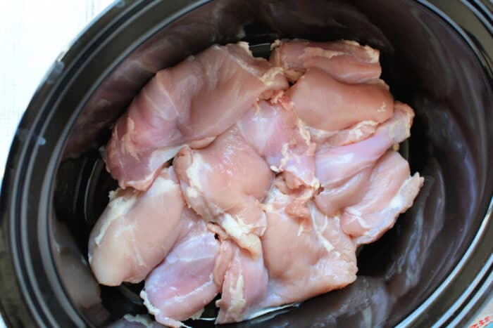 Raw chicken breasts arranged inside a black Crockpot, ready to be cooked into a comforting Crockpot Chicken Pot Pie.