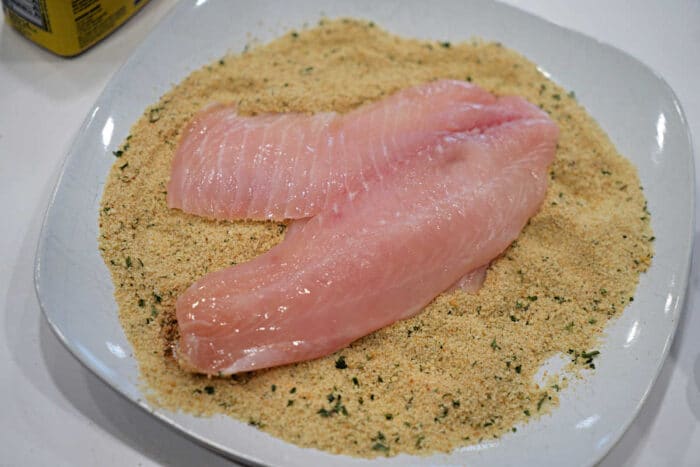 Raw fish fillets on a plate of seasoned bread crumbs, ready for coating and cooking—a classic start to any delicious Fried Tilapia recipe.
