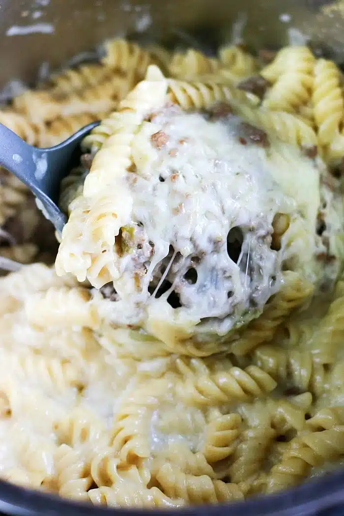 A spoon scoops cheesy, creamy rotini pasta with melted cheese and savory ground meat&mdash;perfect for those craving creative leftover meatloaf recipes.