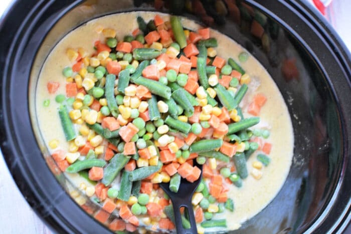 Crockpot Chicken Pot Pie filling with creamy sauce, mixed vegetables, and a black serving spoon.
