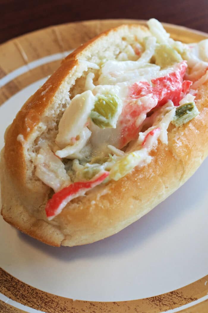 A crab salad sandwich roll filled with creamy crab salad and chopped celery, served on a plate.