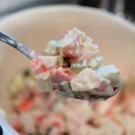 A spoonful of creamy crab salad with diced vegetables is held above a white bowl, perfect for a fresh Crab Salad Sandwich.