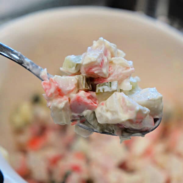 A spoonful of creamy crab salad with diced vegetables is held above a white bowl, perfect for a fresh Crab Salad Sandwich.
