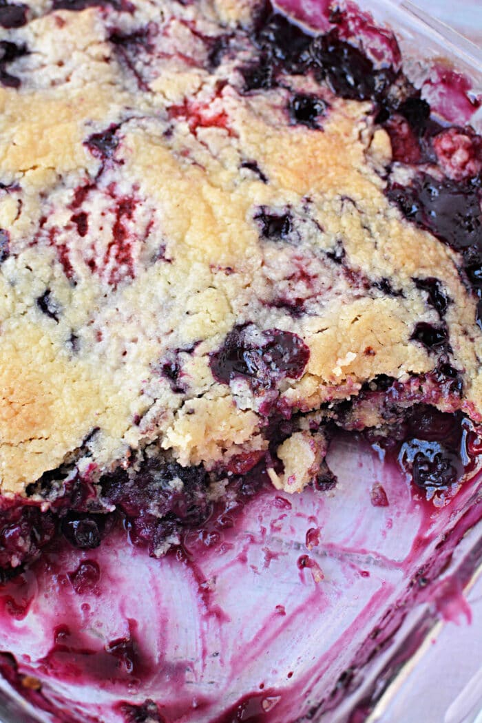 A close-up of a partially eaten berry cobbler with cake mix in a glass baking dish.